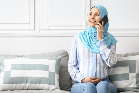Pregnant Muslim woman talking by mobile phone at home