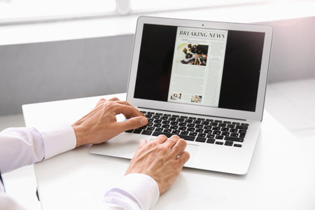 Young businessman reading newspaper online in officeの写真素材