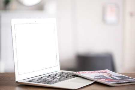 Modern laptop with magazine on table in roomの写真素材