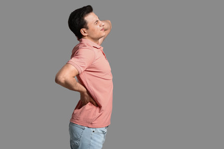 Young man suffering from back pain on gray background