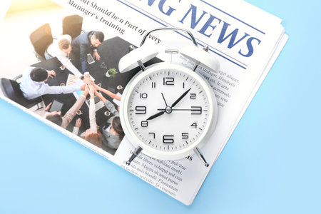 Stylish alarm clock and newspaper on color background