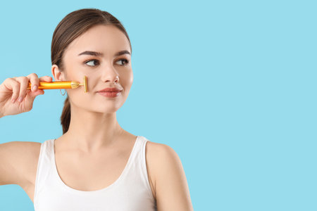 Beautiful young woman with facial massage tool on color background