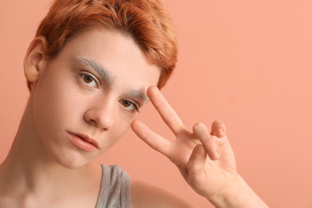 Teenage boy with dyed eyebrows showing victory gesture on color backgroundの写真素材