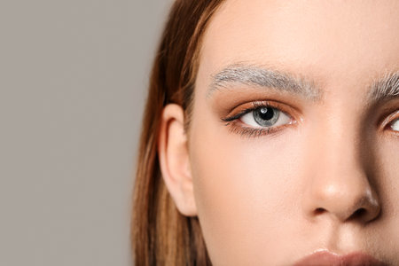 Beautiful young woman with dyed eyebrows on gray backgroundの写真素材