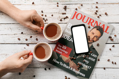 Man with cups of coffee, magazine and mobile phone on white wooden background
