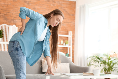 Young woman suffering from back pain at homeの写真素材