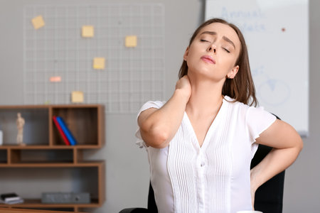 Young woman suffering from back pain in officeの写真素材