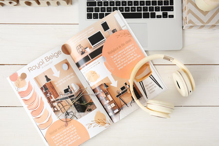 Modern headphones with magazine and laptop on table