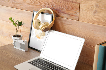 Laptop with headphones and picture on table near wooden wallの写真素材