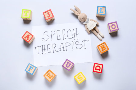 Paper with text SPEECH THERAPIST, toy and cubes on light backgroundの写真素材