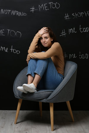 Stressed young woman sitting near dark wall with written hashtags. concept of harassmentの写真素材