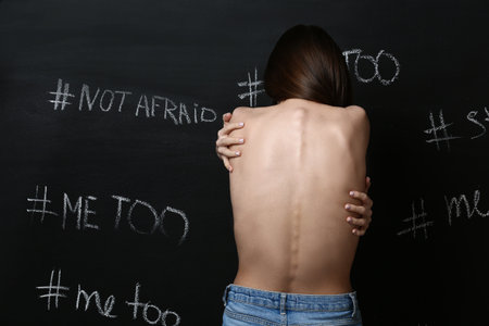 Young woman near dark wall with written hashtags. concept of harassment
