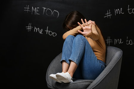 Stressed young woman sitting near dark wall with written hashtags. concept of harassmentの写真素材