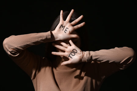 Stressed young woman with text ME TOO written on her palms against dark background. concept of harassmentの写真素材