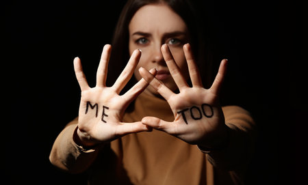 Stressed young woman with text ME TOO written on her palms against dark background. concept of harassmentの写真素材