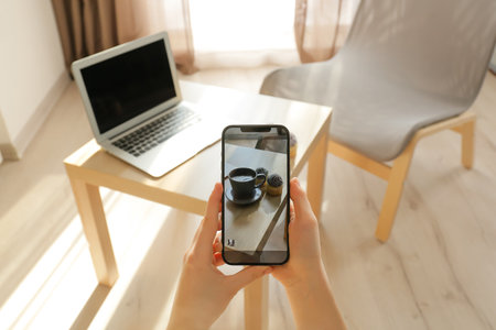 Woman taking photo of coffee cup and cupcakes in room
