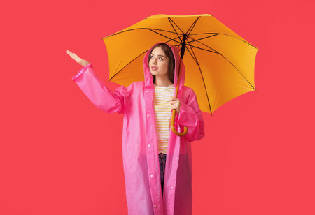 Stylish young woman in raincoat and umbrella on color backgroundの写真素材