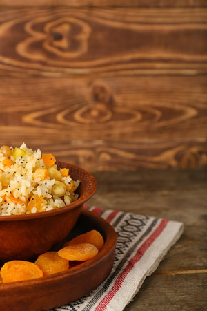 Tray with bowl of rice Kutya and dried apricots on wooden table, closeupの写真素材