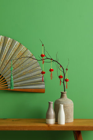 Vases with tree branches and decor for Chinese New Year celebration on bench near green wallの写真素材