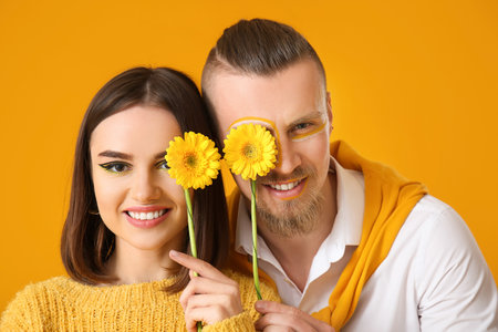 Stylish young couple with flowers on yellow backgroundの写真素材