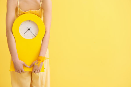 Stylish young woman with clock on yellow background