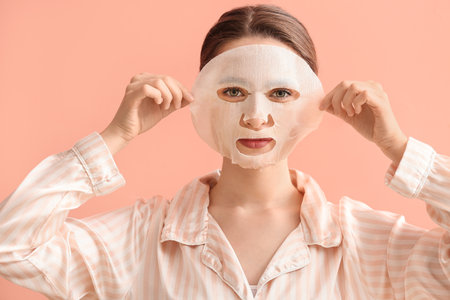 Beautiful young woman with sheet facial mask on color backgroundの写真素材