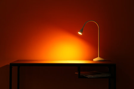 Glowing lamp and newspapers on table in dark room