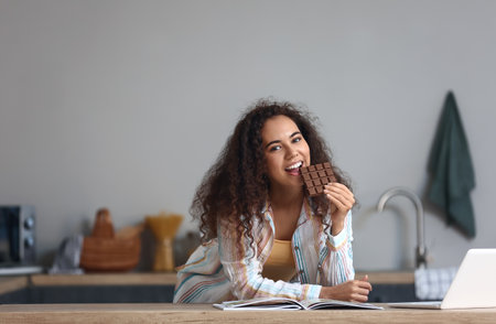 Young African-American woman eating chocolate in the kitchen