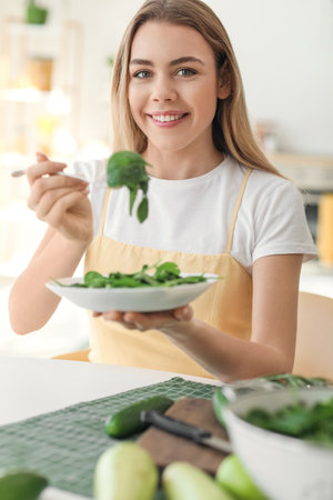 Young woman eating fresh salad in the kitchenの写真素材