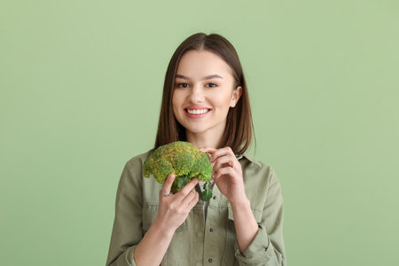Young woman with fresh broccoli on color backgroundの写真素材