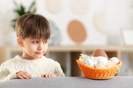 Cute little boy with basket of chocolate Easter eggs at home