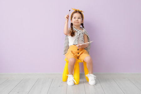 Cute little artist sitting near color wall
