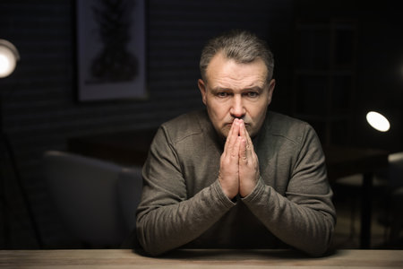 Praying mature man in dark room