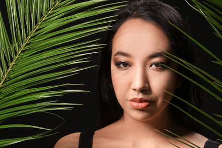 Beautiful Asian woman with tropical leaves on dark backgroundの写真素材