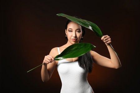 Beautiful Asian woman with tropical leaves on dark background