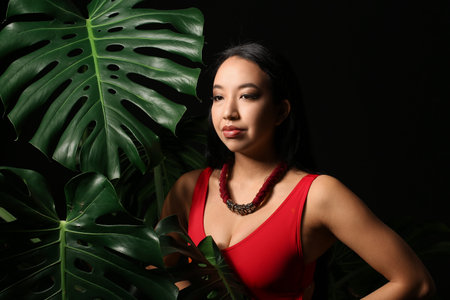 Beautiful Asian woman and tropical leaves on dark backgroundの写真素材