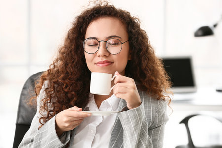 Beautiful young woman drinking coffee in officeの写真素材