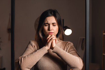Religious young woman praying to God at home in the eveningの写真素材