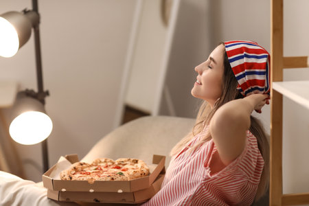 Beautiful young woman with tasty pizza relaxing at home in the eveningの写真素材