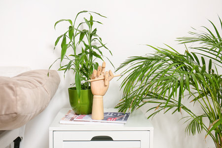 Wooden hand with magazines and houseplants on table near light wallの写真素材