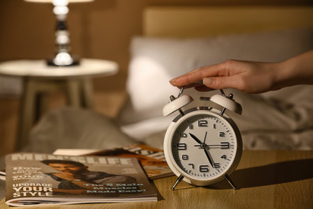 Woman with alarm clock in bedroom at nightの写真素材