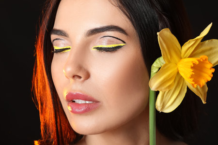 Beautiful young woman with stylish makeup and flower on dark backgroundの写真素材