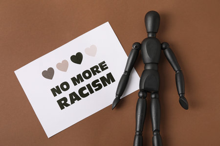 Black mannequin and paper sheet with text NO MORE RACISM on color backgroundの写真素材