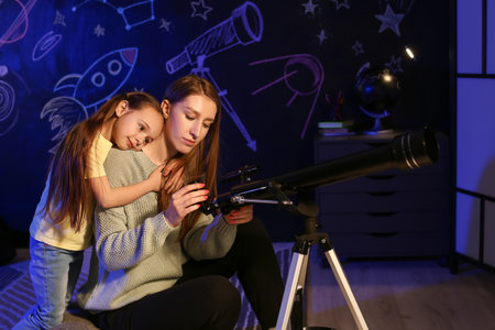 Cute little girl and her mother with telescope looking at stars in the eveningの写真素材