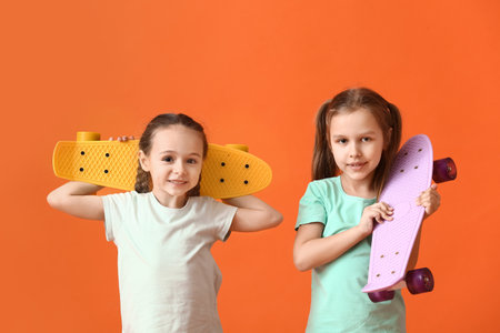 Cute little sisters with skateboards on color backgroundの写真素材