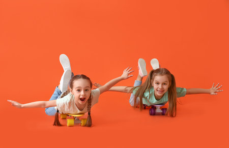 Cute little sisters with skateboards on color background