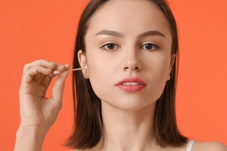 Young woman cleaning ears with cotton bud on color background, closeup