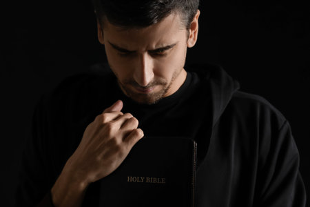 Religious young man with Bible praying on dark backgroundの写真素材