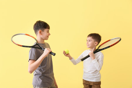 Portrait of cute brothers with tennis rackets and ball on color backgroundの写真素材