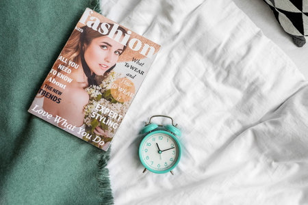 Alarm clock with magazine on bedの写真素材